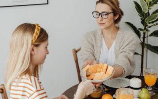Mother and daughter enjoying a healthy breakfast together with fresh fruits and juice.