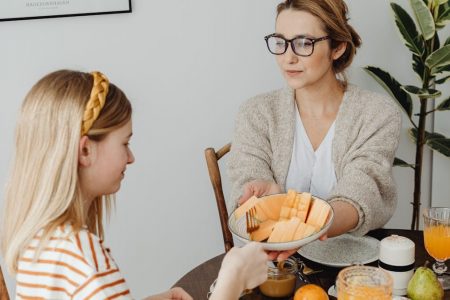 Mother and daughter enjoying a healthy breakfast together with fresh fruits and juice.